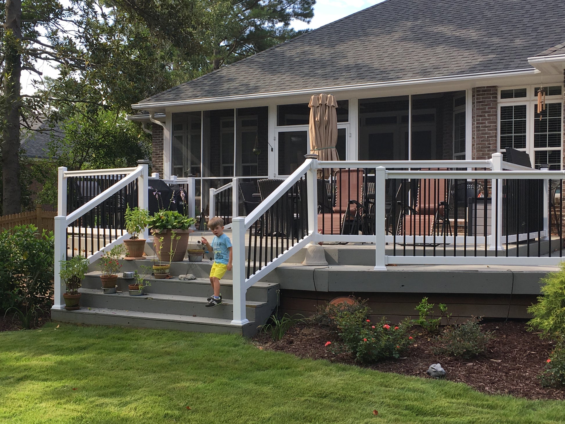 House with a white deck, surrounded by greenery and a small child dreaming of one day owning his own Weatherables Birmingham white vinyl deck and stair railings