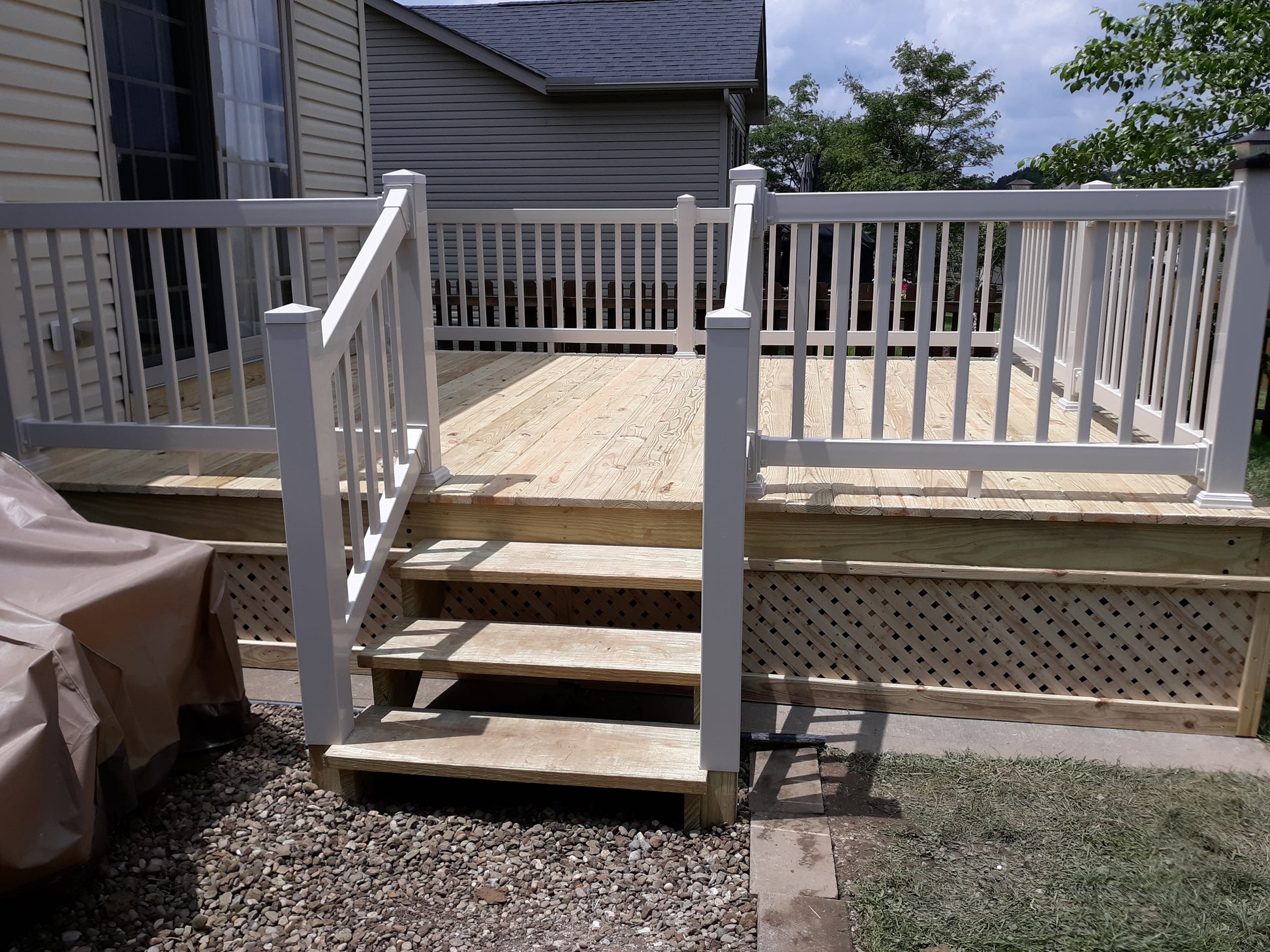 Wooden deck with Weatherables Greenwich white vinyl deck railings and steps leading to a house.