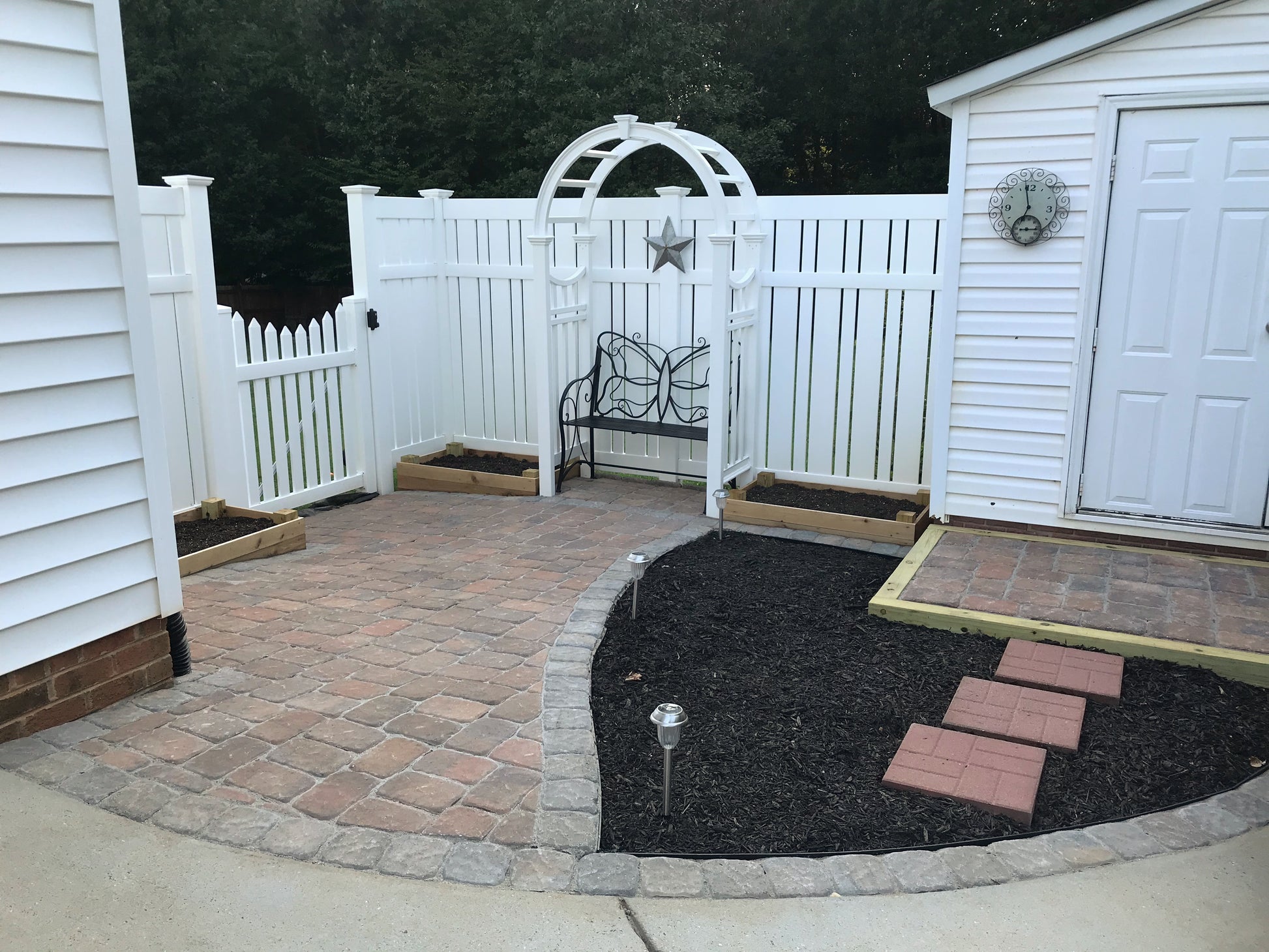 Backyard patio with paved area, garden bed, and Weatherable Alden white vinyl semi-privacy fence.