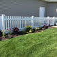 Lawn with a Weatherables Chelsea white vinyl picket fence and garden bed in front of a house.