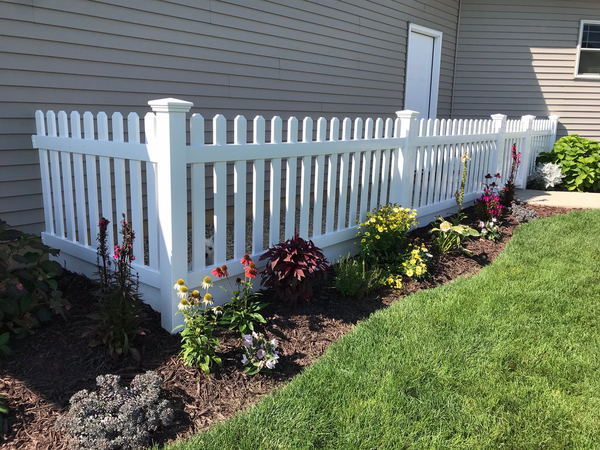 Weatherables Chelsea white vinyl picket fence with garden bed in front of a house