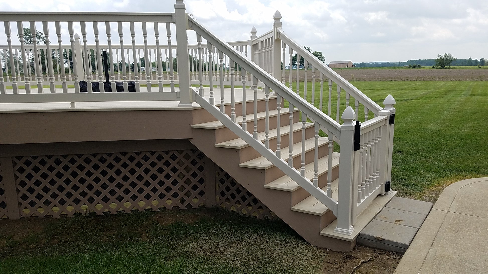 Weatherables Addison white vinyl stair railing on a  staircase leading to a deck with a grassy area and cloudy sky in the background