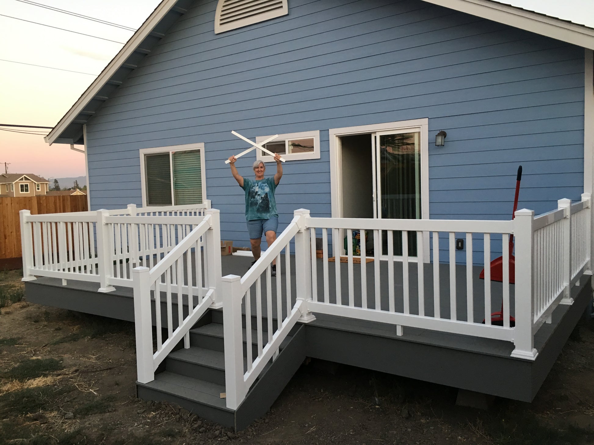 Person holding vinyl balusters on a blue house with white deck with a Weatherables Greenwich white vinyl deck railing.