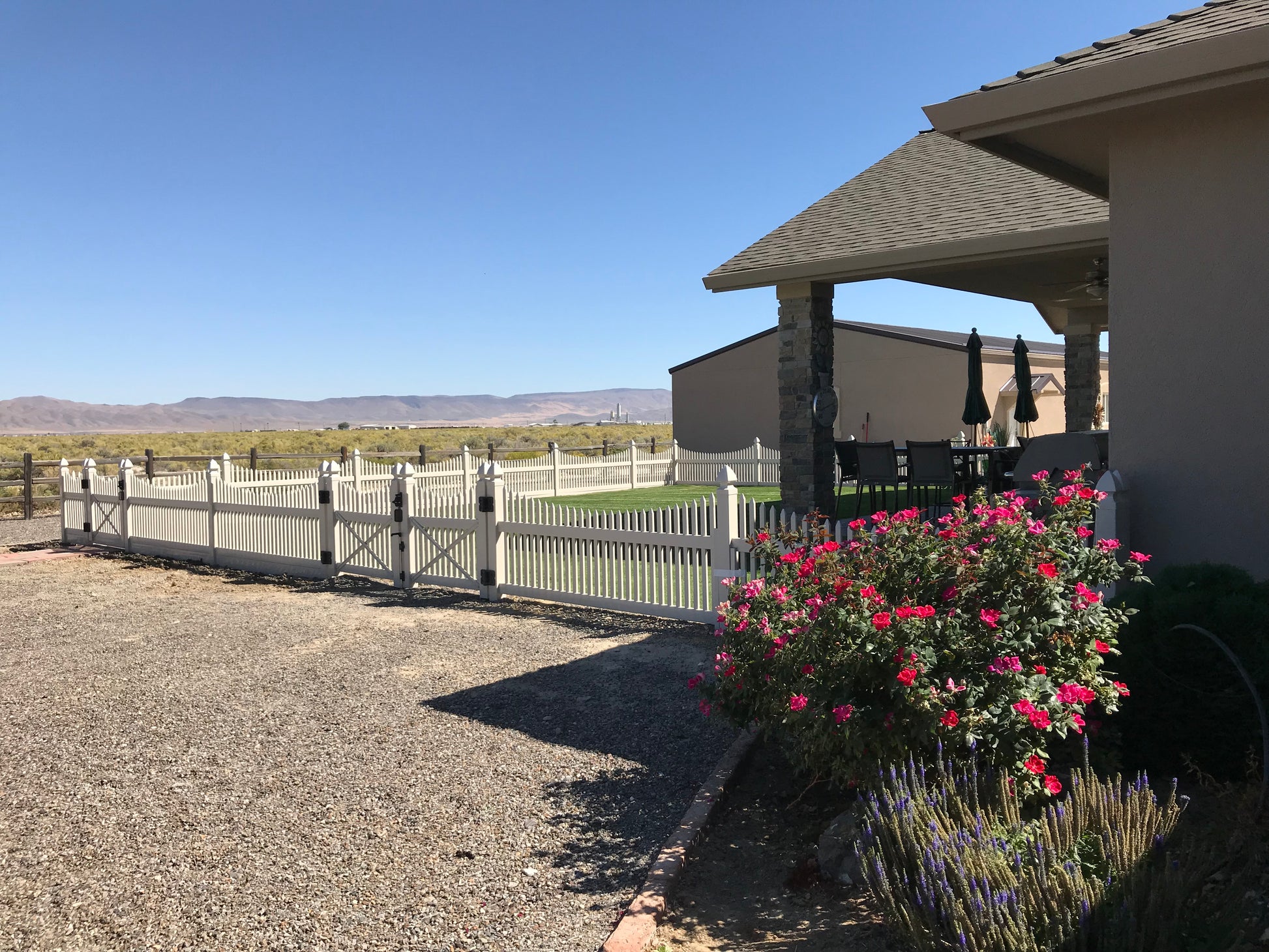 House exterior with a Weatherables Barrington tan vinyl picket fence and flowering plants on a clear day.
