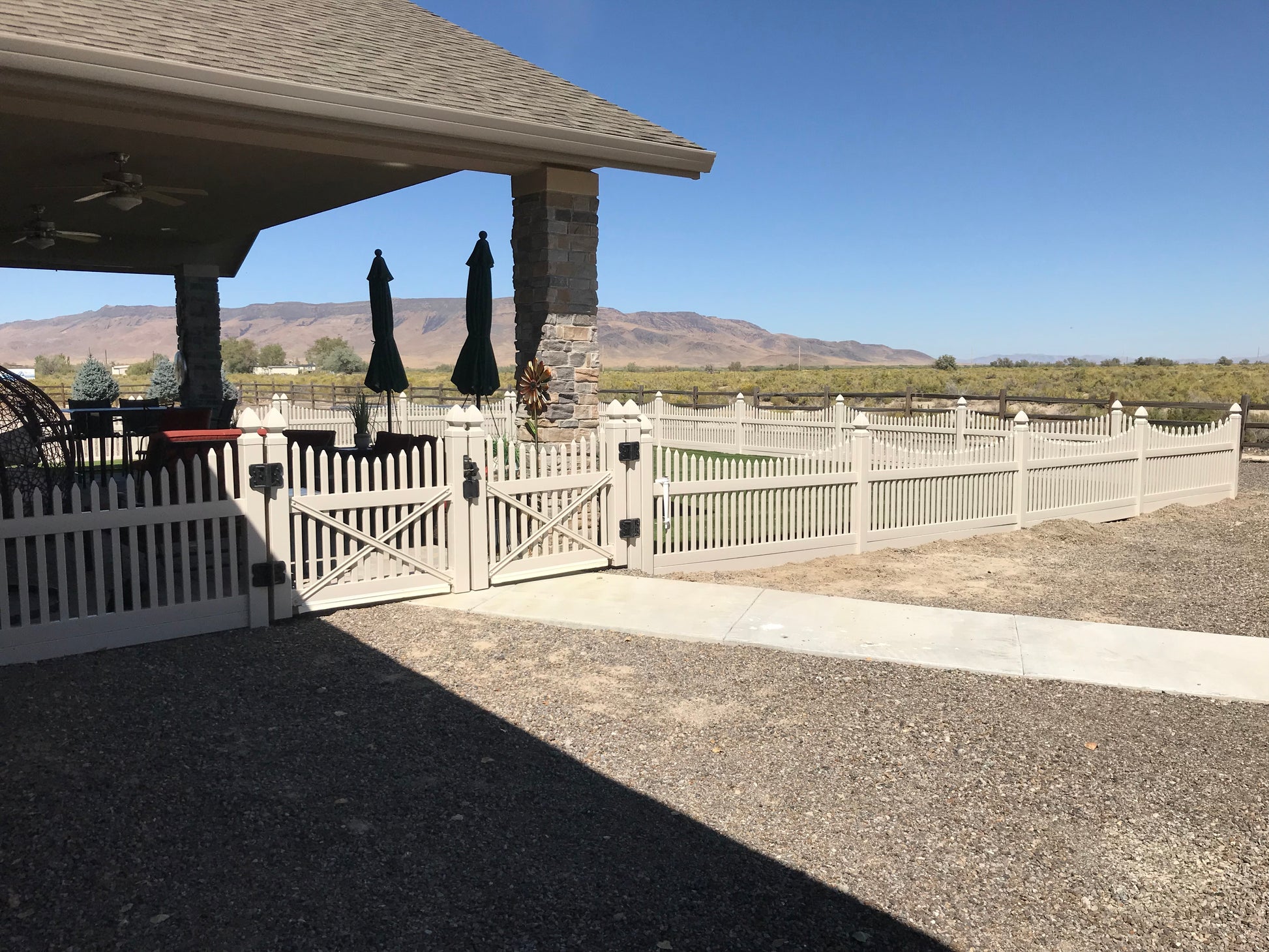 Patio area with a gazebo, outdoor furniture, Weatherables Barrington tan vinyl scalloped picket fence and a scenic background.