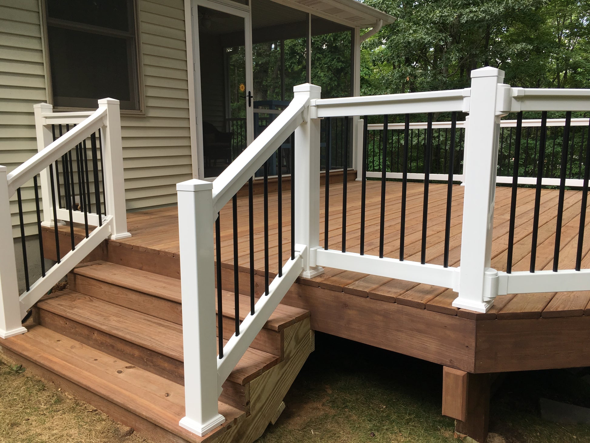 Wooden deck with Weatherables Wiltshire white vinyl deck railing featuring black metal balusters, leading to a house.