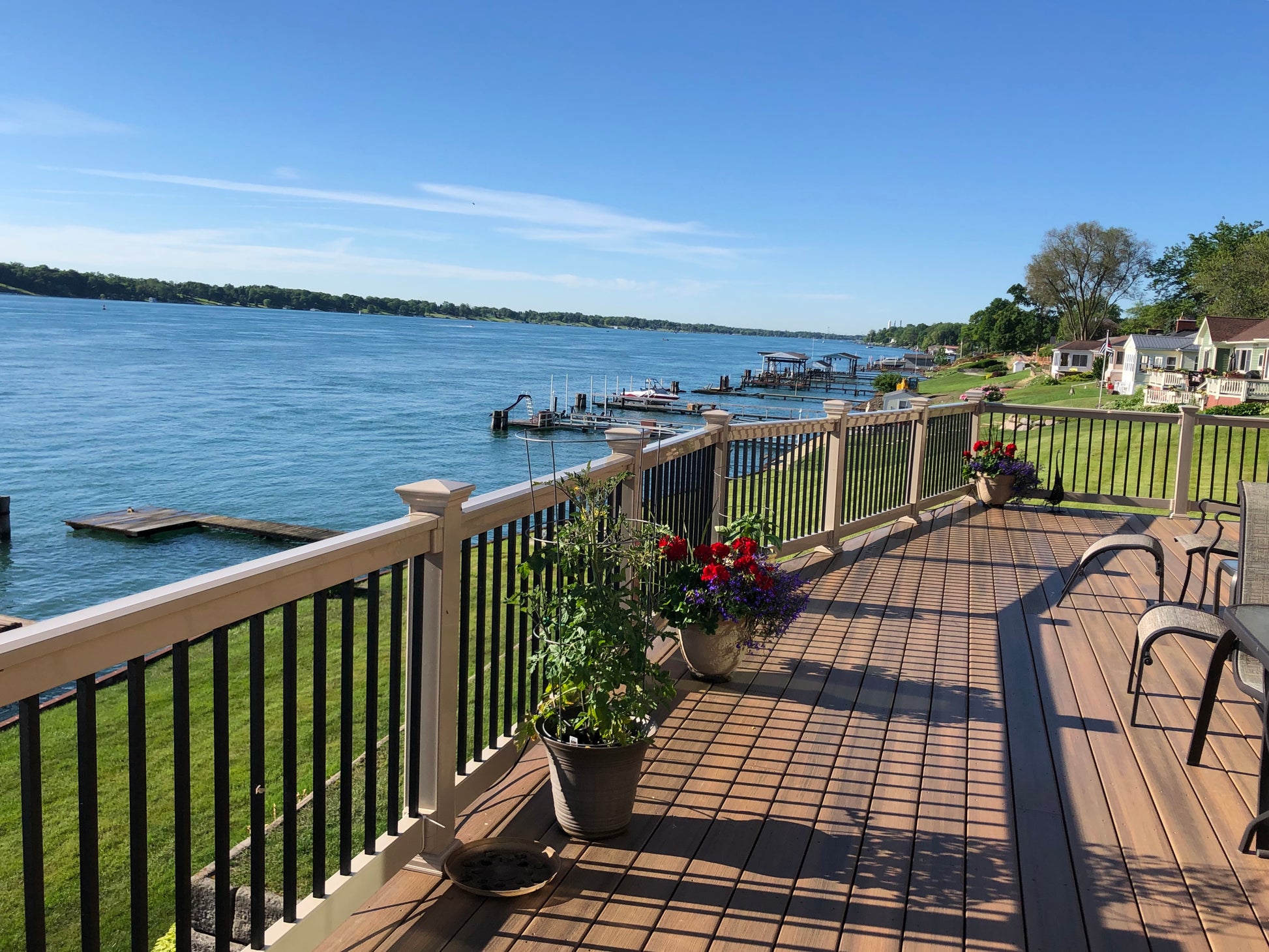 Deck and Weatherables Birmingham khaki vinyl deck railing overlooking a lake with potted plants and chairs on a sunny day.