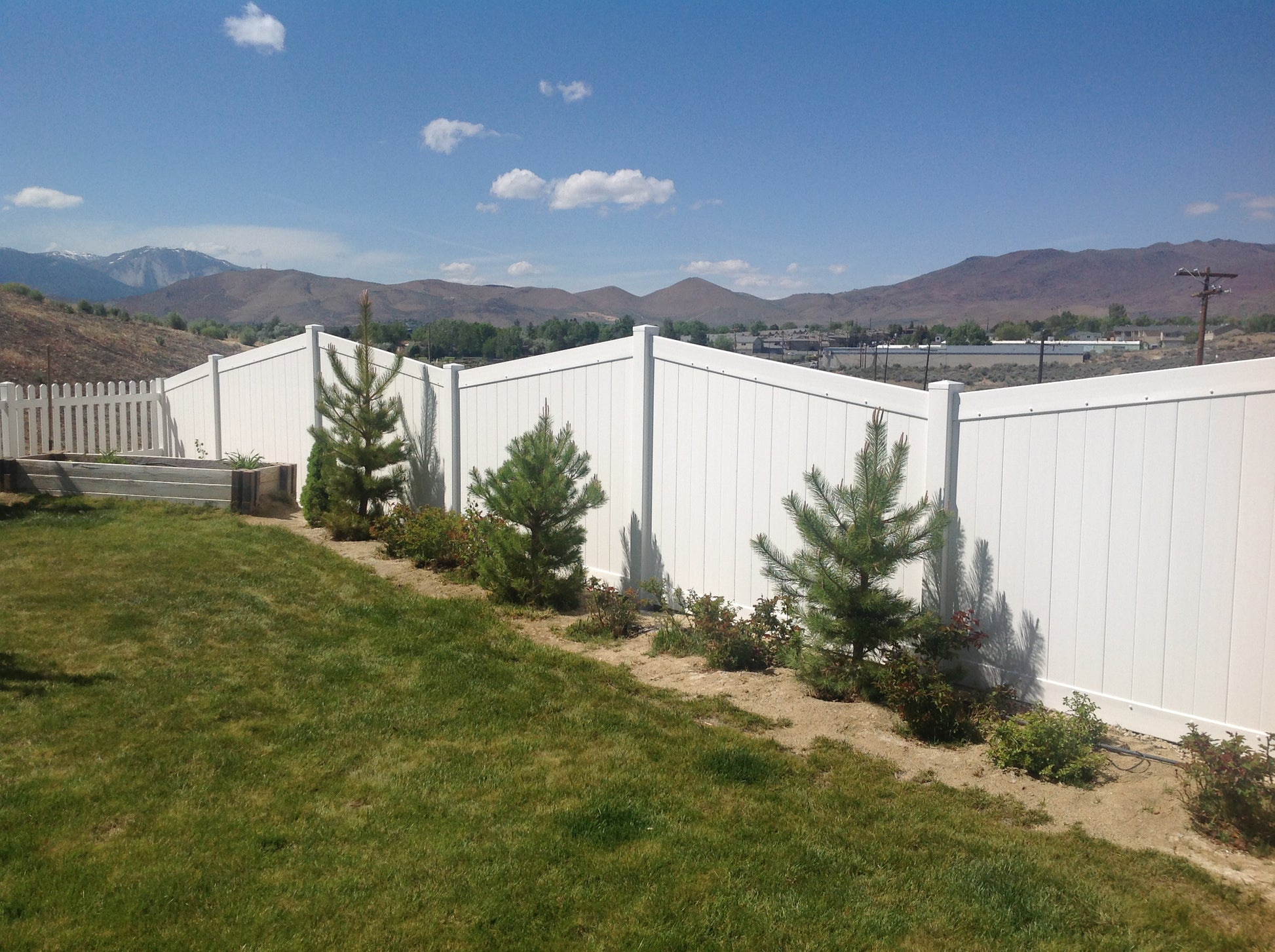Weatherables Pembroke white vinyl privacy fence with greenery and mountains in the background