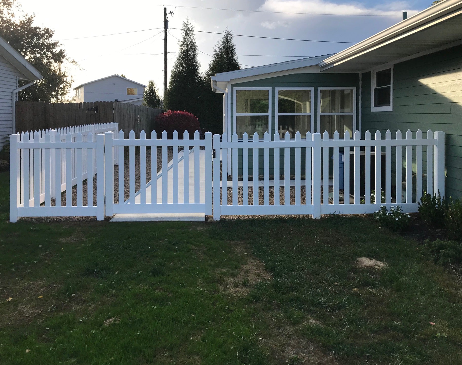 Weatherables white vinyl picket fence in front of a house with green grass and trees in the background.