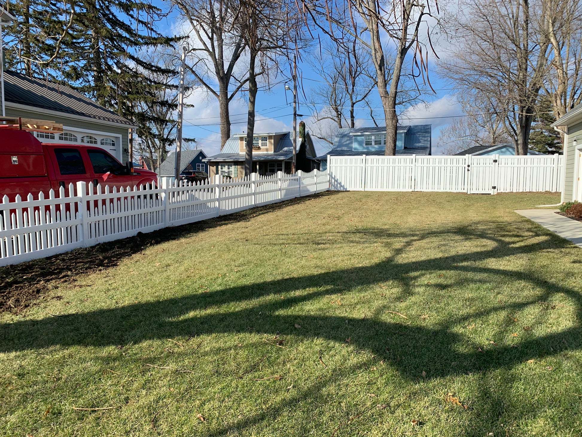 Backyard with Weatherables Alden white vinyl semi-privacy fence, grass, and trees on a clear day.