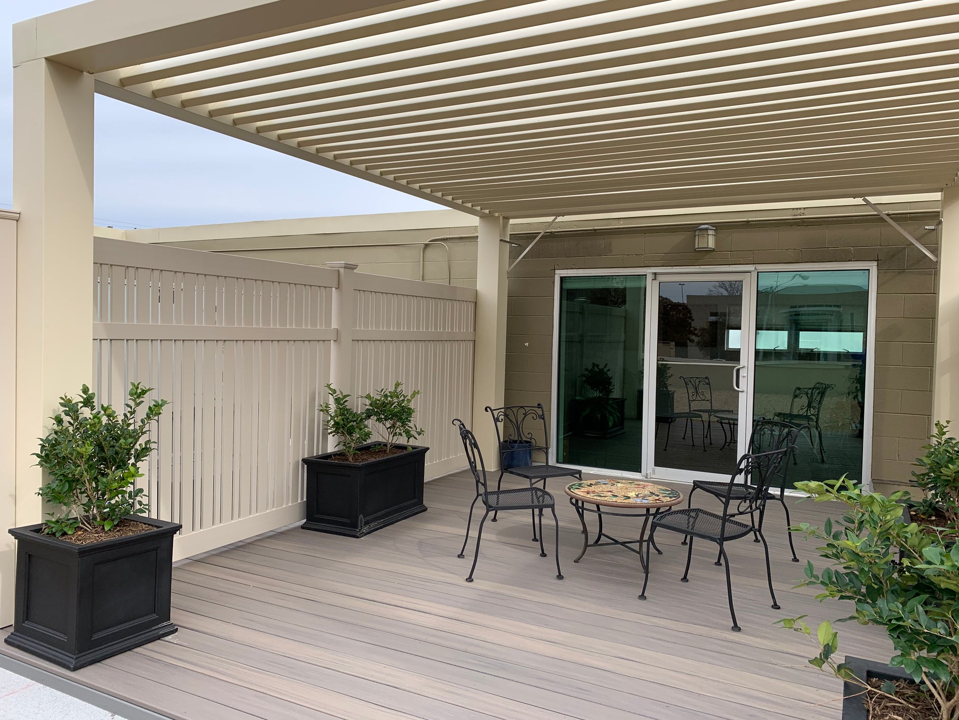 Outdoor patio area with Weatherables Davenport tan vinyl semi-privacy fencing,  pergola, table, chairs, and plants.