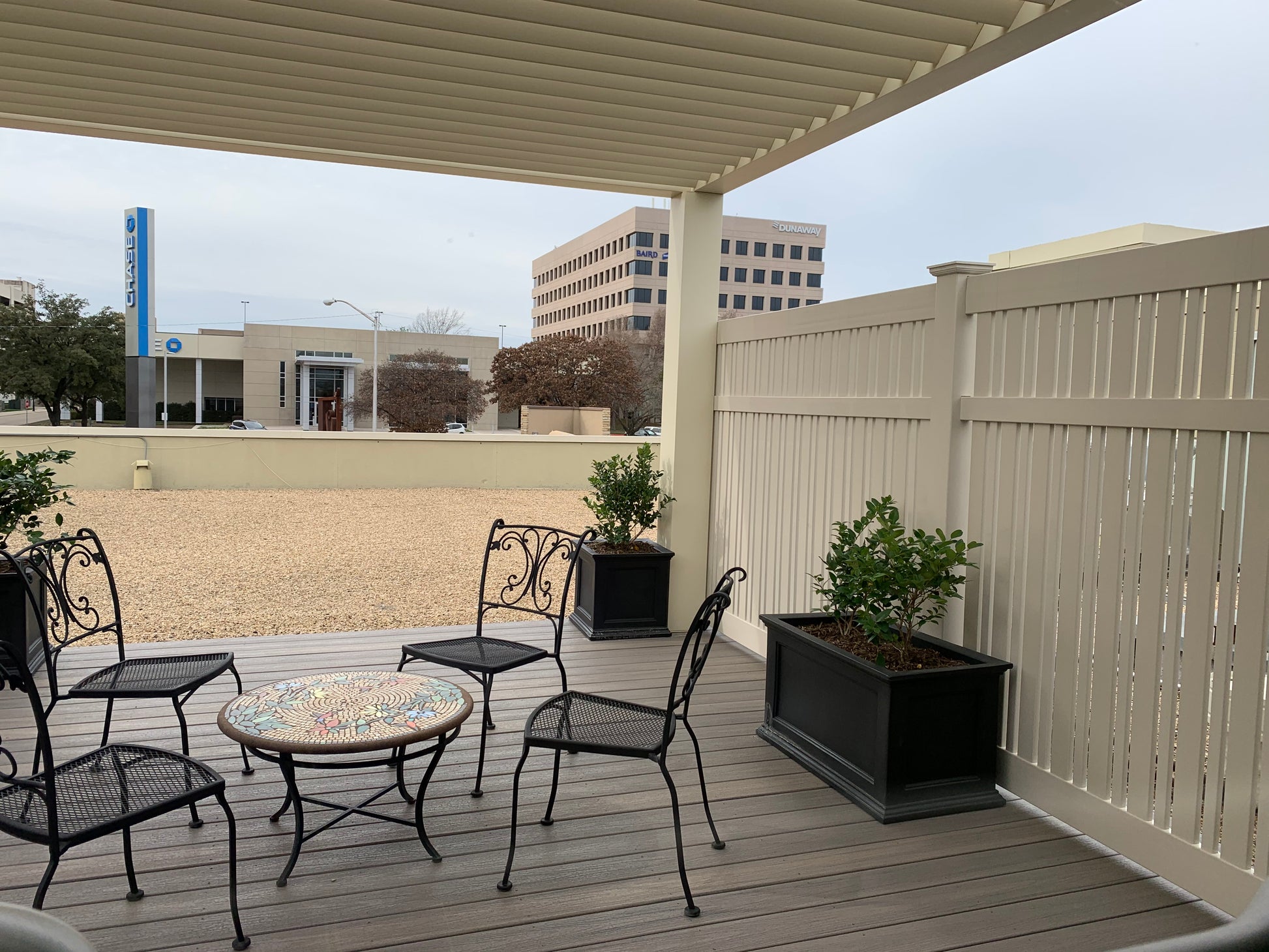 Outdoor patio area with Weatherables Davenport tan vinyl semi-privacy fencing chairs, table, and plants under a covered deck.