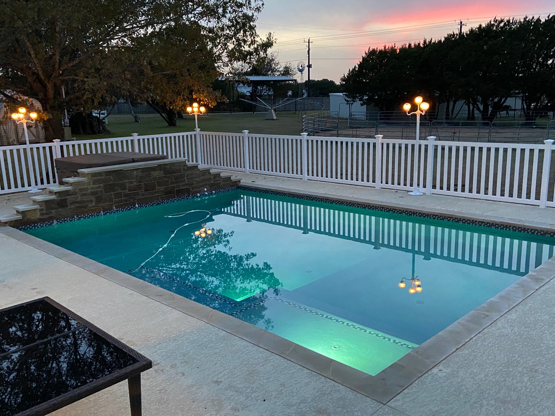 Pool area with a Weatherables Captiva white vinyl closed-top picket fence, trees, and a sunset sky.