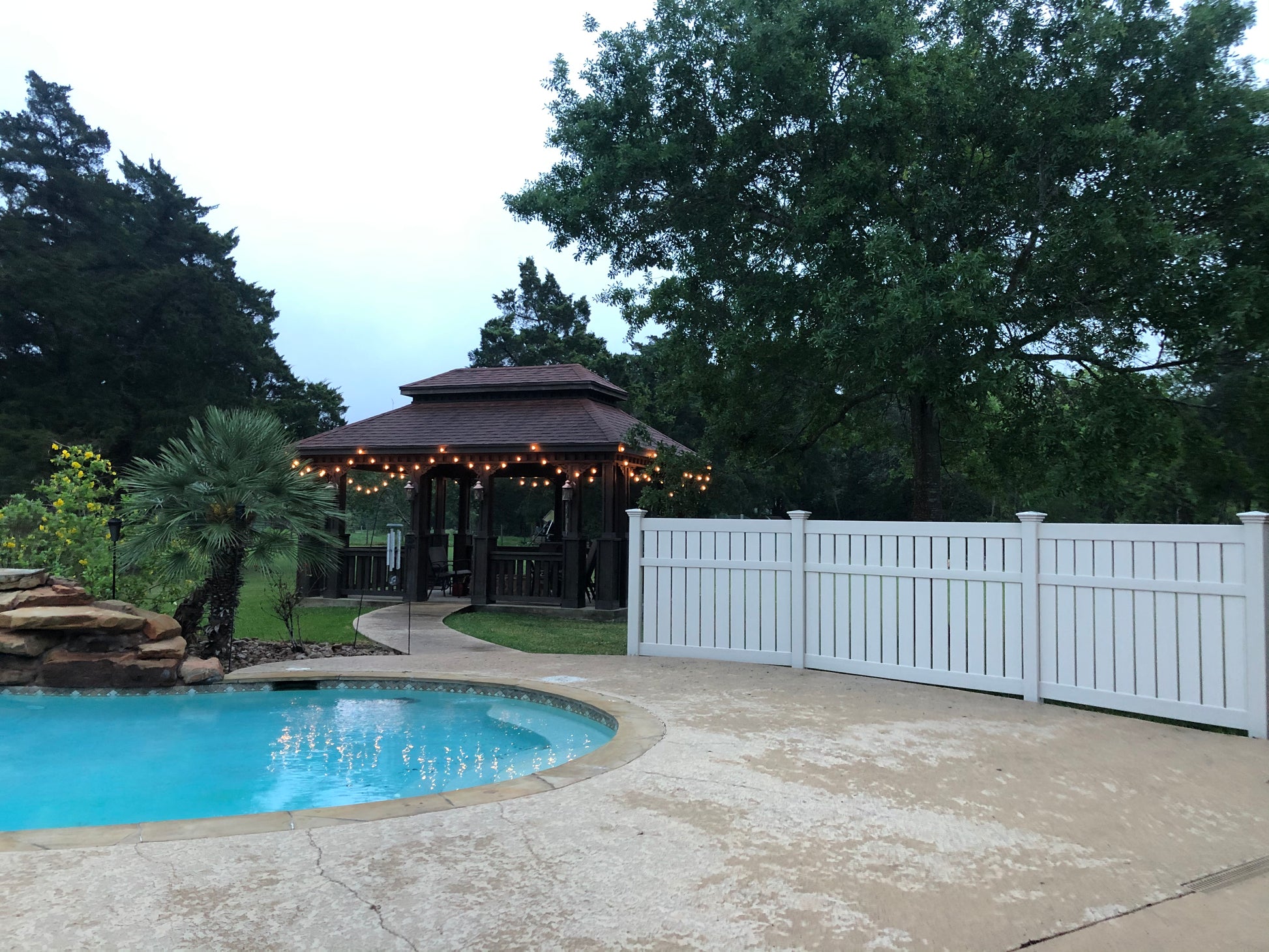 Pool area with a gazebo and Weatherables white vinyl semi-privacy fence surrounded by trees