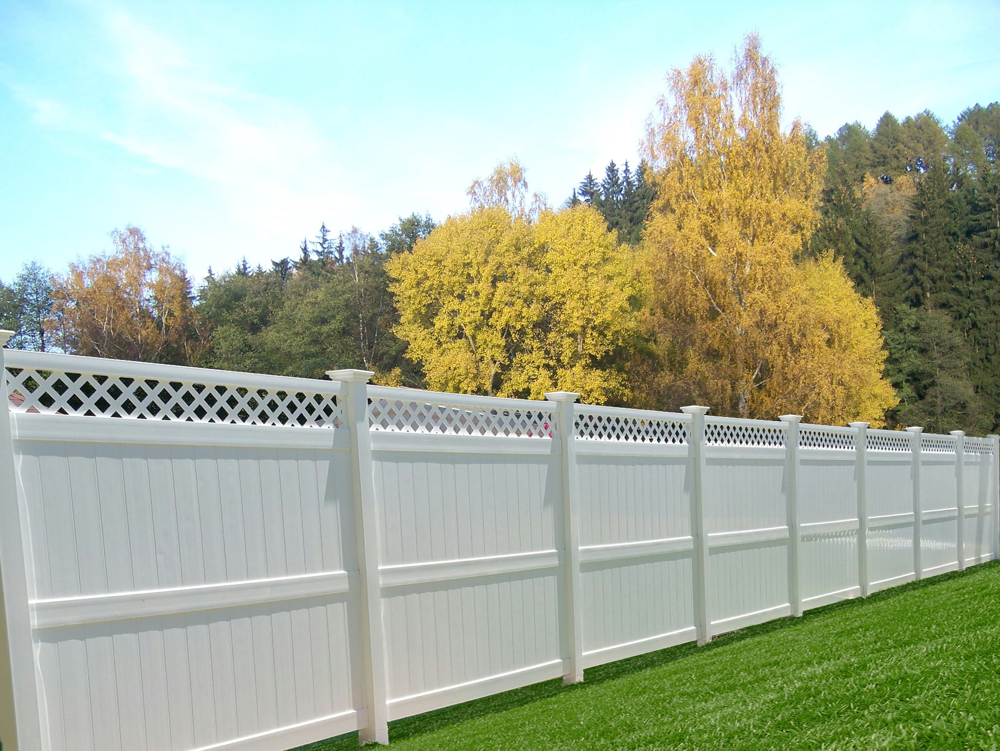 Weatherables Ashton white vinyl  privacy fence with lattice top in a backyard setting with trees and grass.