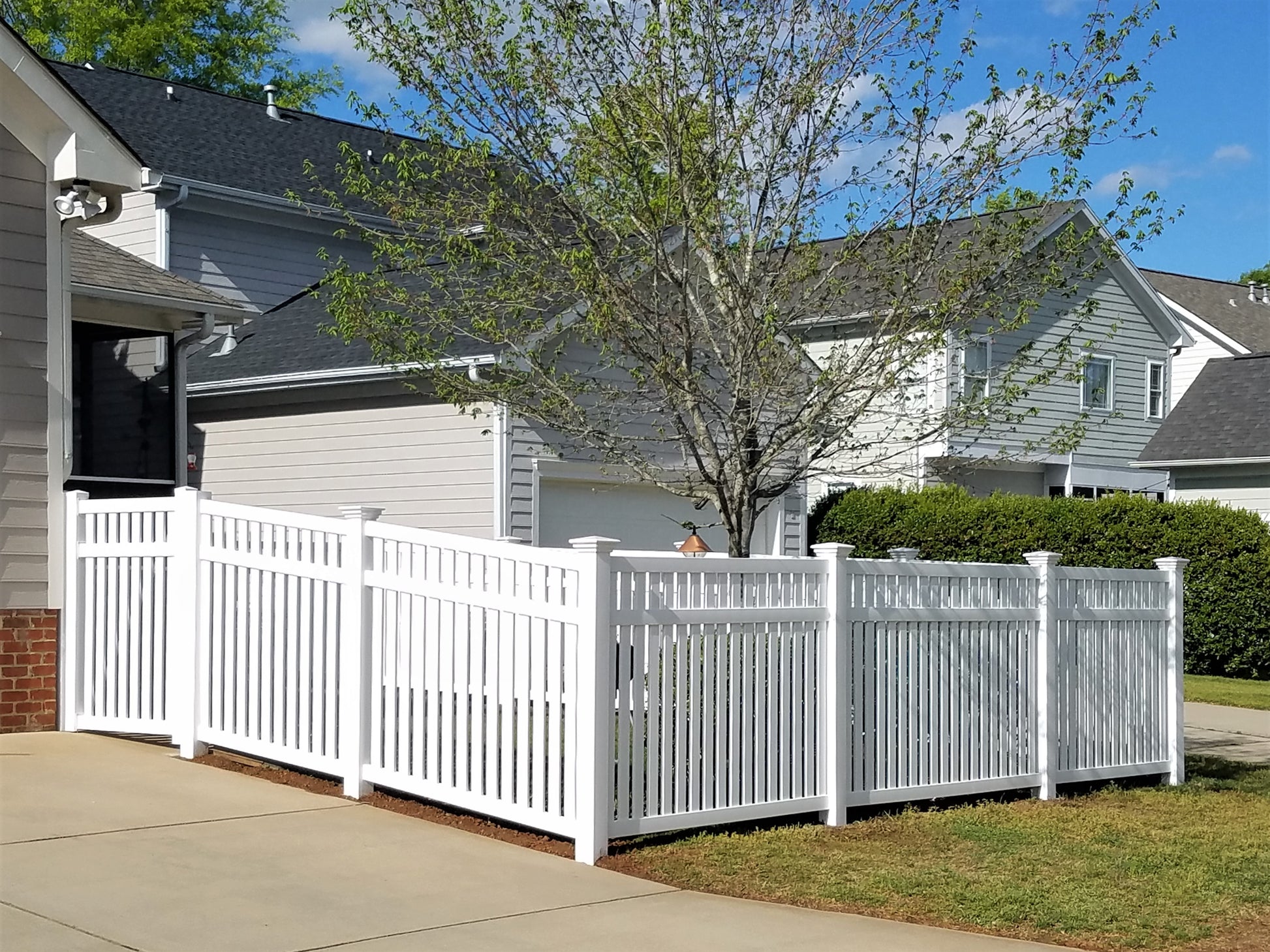 Weatherables Crestview white vinyl pool fence in front of a house with trees and blue sky.