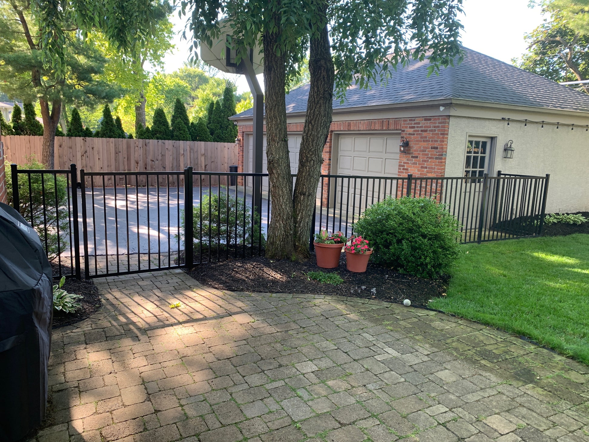 Driveway with a black aluminum Weatherables Atlantic fence and gate, potted plants, and a house in the background.