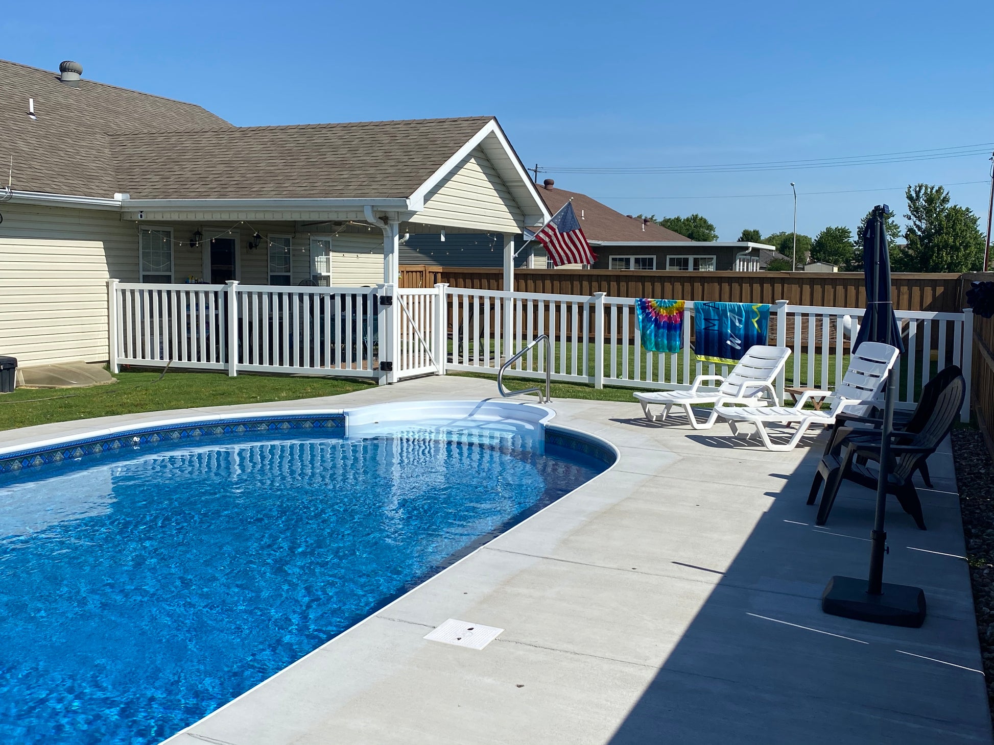 Pool area surrounded by Weatherables Captiva white vinyl pool fence with lounge chairs, towels, and a house in the background
