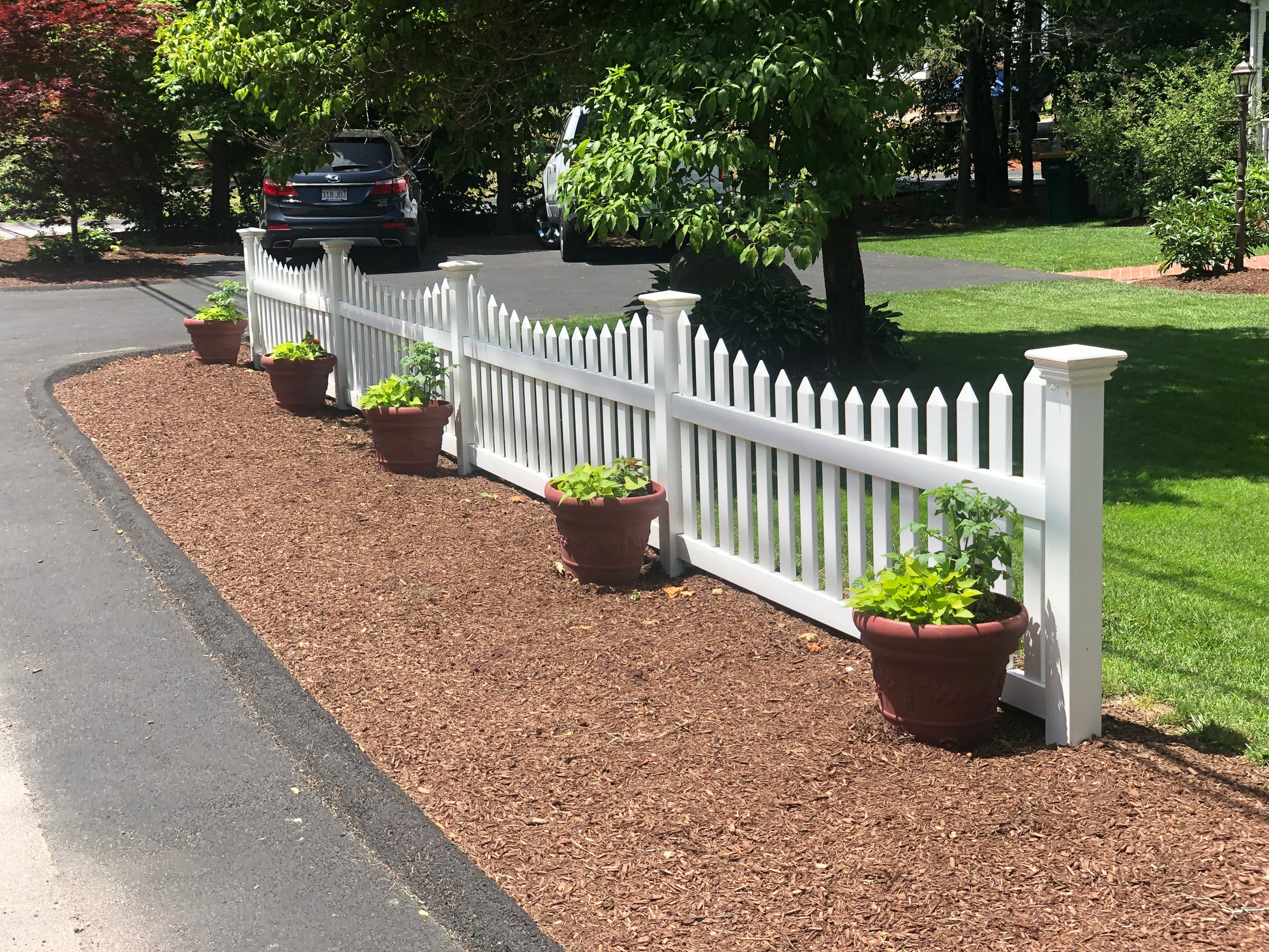 Weatherables Ellington white vinyl picket fence with potted plants along a driveway