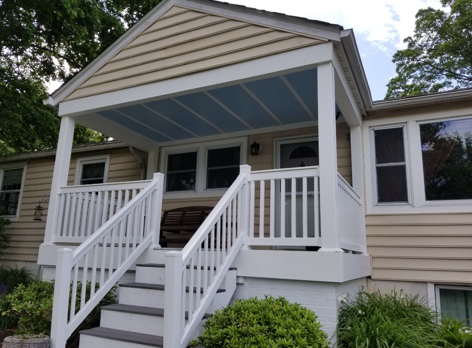 Front porch of a house with Weatherables Yorkshire white vinyl deck railings and steps, surrounded by greenery.