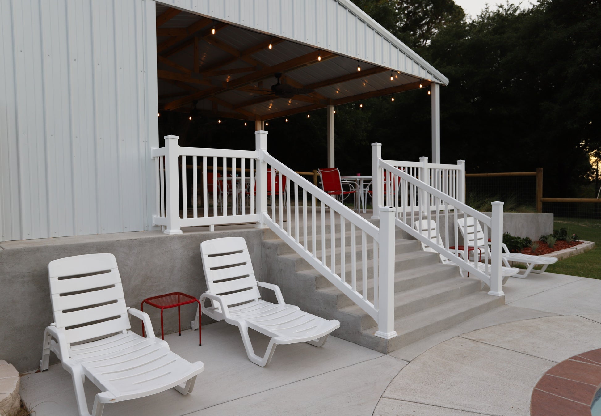 White lounge chairs on a patio with a covered outdoor area in the background.