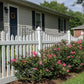 Weatherables Hampshire white vinyl picket fence with flowering bushes in front of a house