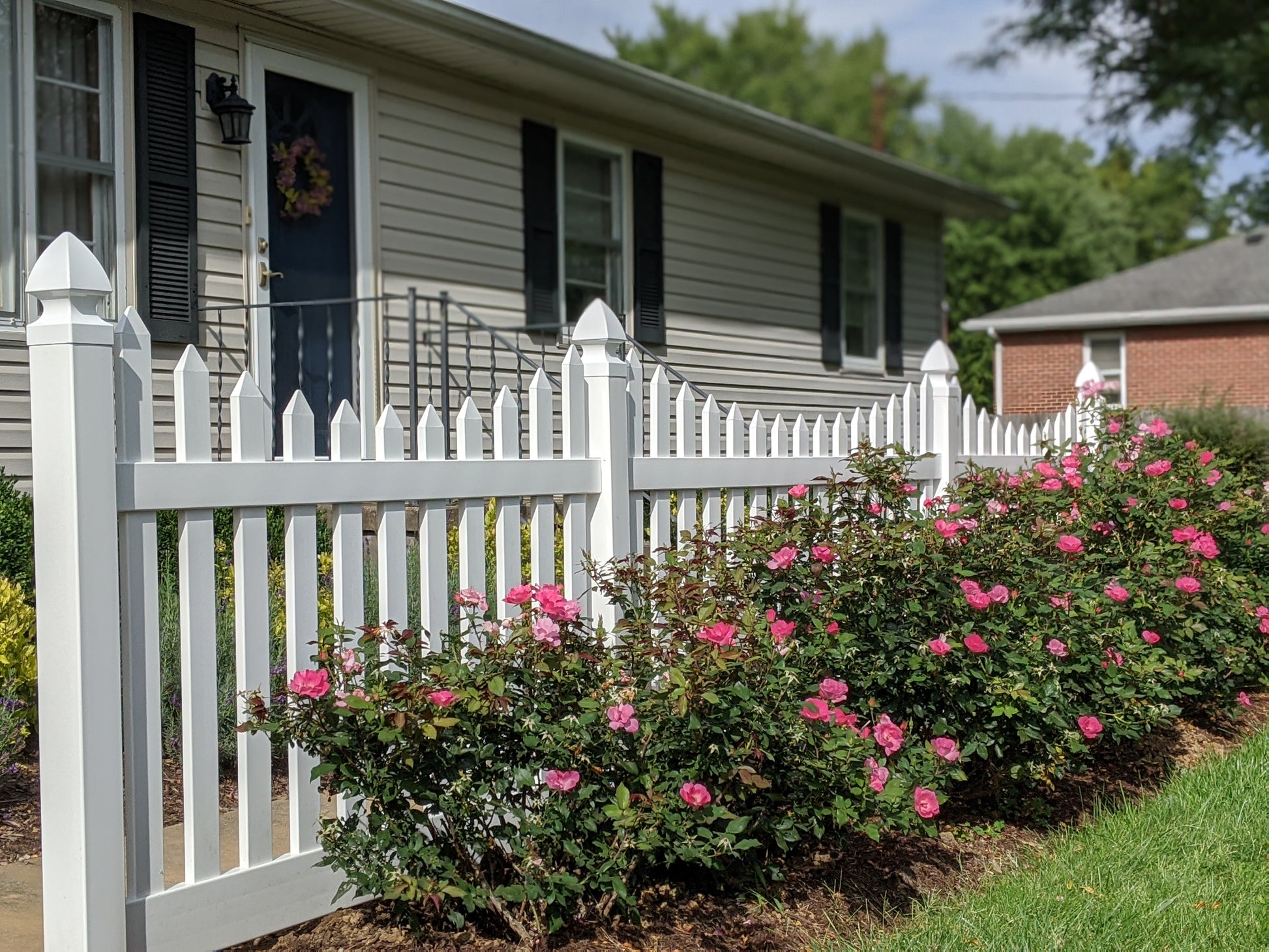 Weatherables Hampshire white vinyl picket fence with flowering bushes in front of a house