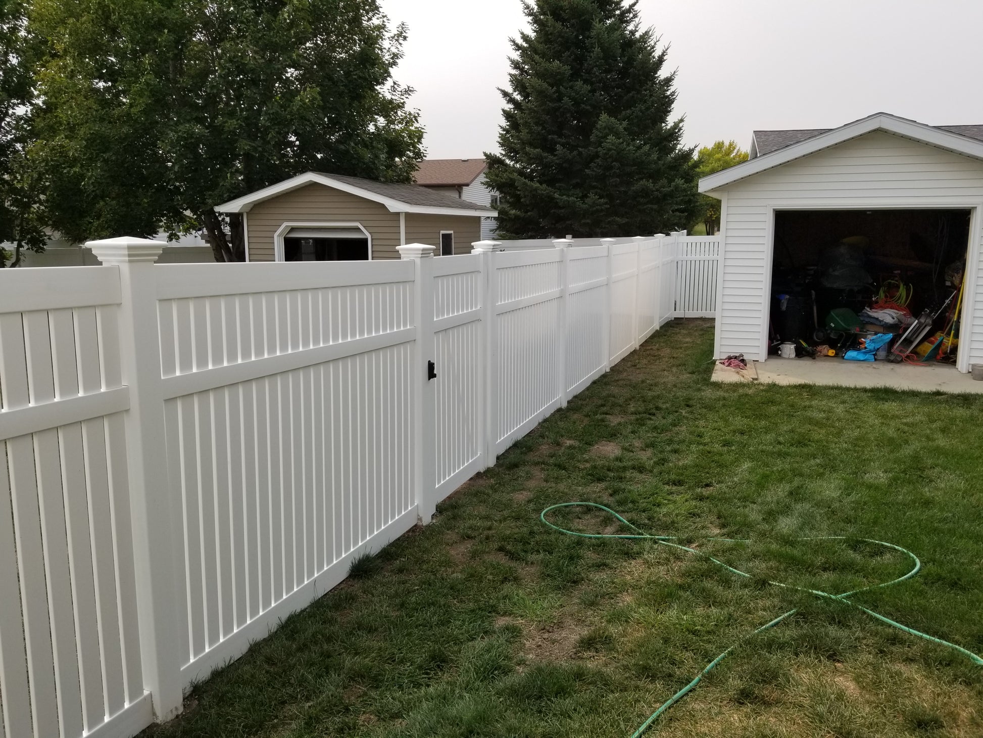 Weatherables Huntington white vinyl semi-privacy fence along a grassy area with a shed and trees in the background.