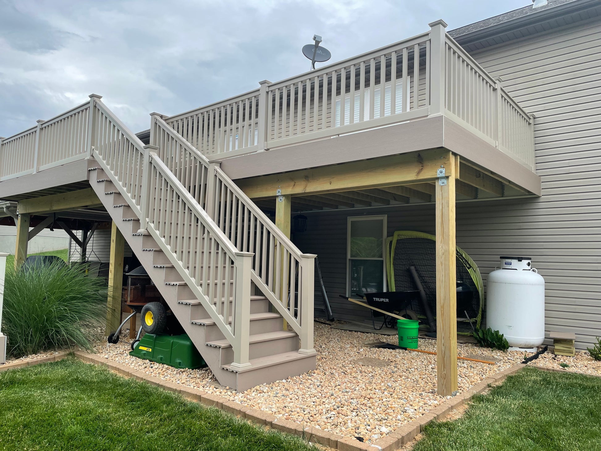Wooden deck with stairs and Weatherables Washington khaki vinyl and stair railing leading up to it, attached to a house with a cloudy sky.