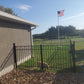 American flag on a flagpole in front of a building with a Weatherables Toledo black aluminum gate and grassy area fencing in a dog.