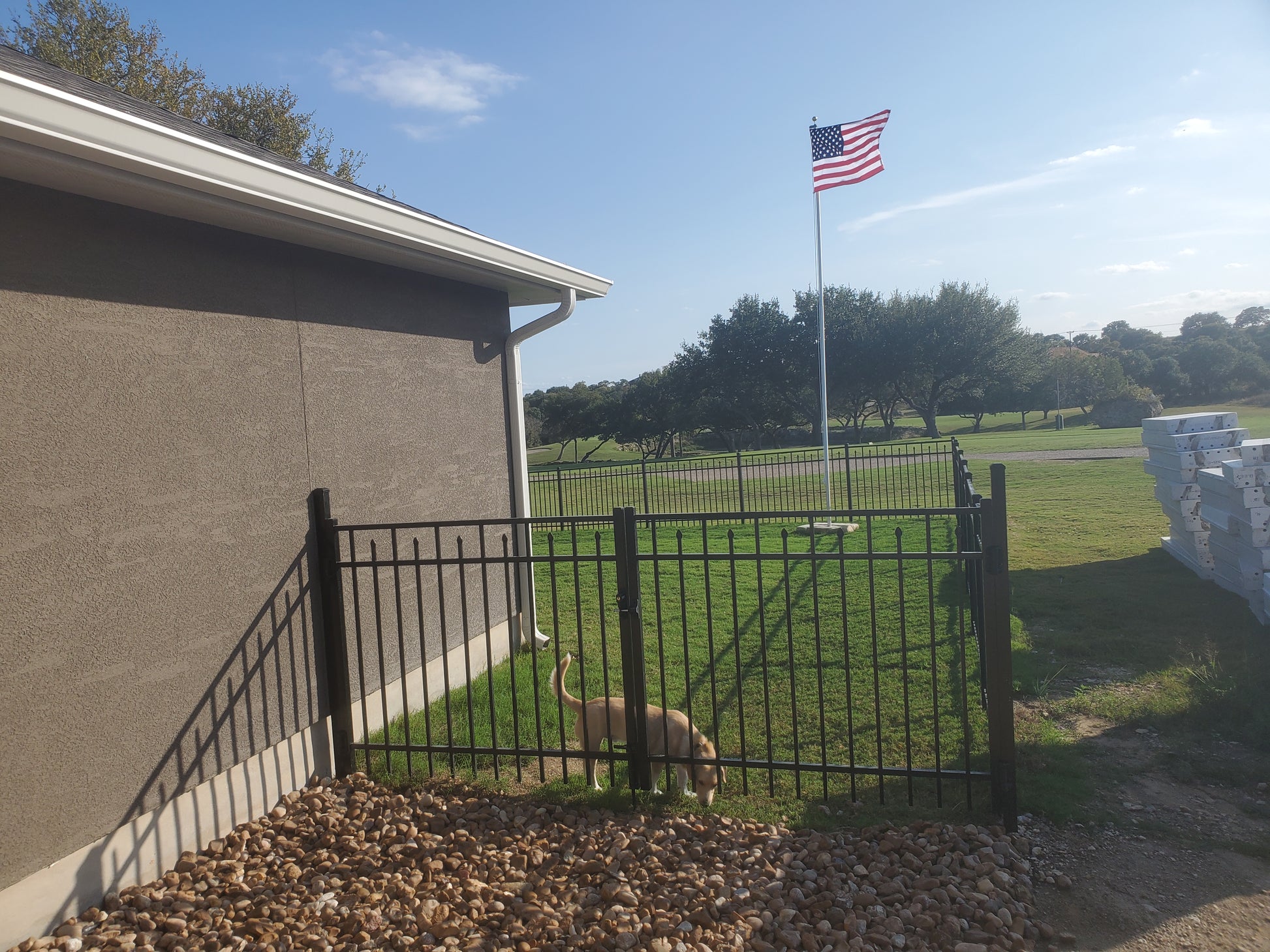 American flag on a flagpole in front of a building with a Weatherables Toledo black aluminum gate and grassy area fencing in a dog.