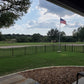 American flag on a flagpole in a park with trees and a clear sky behind a Weatherables Toledo black aluminum fencing.