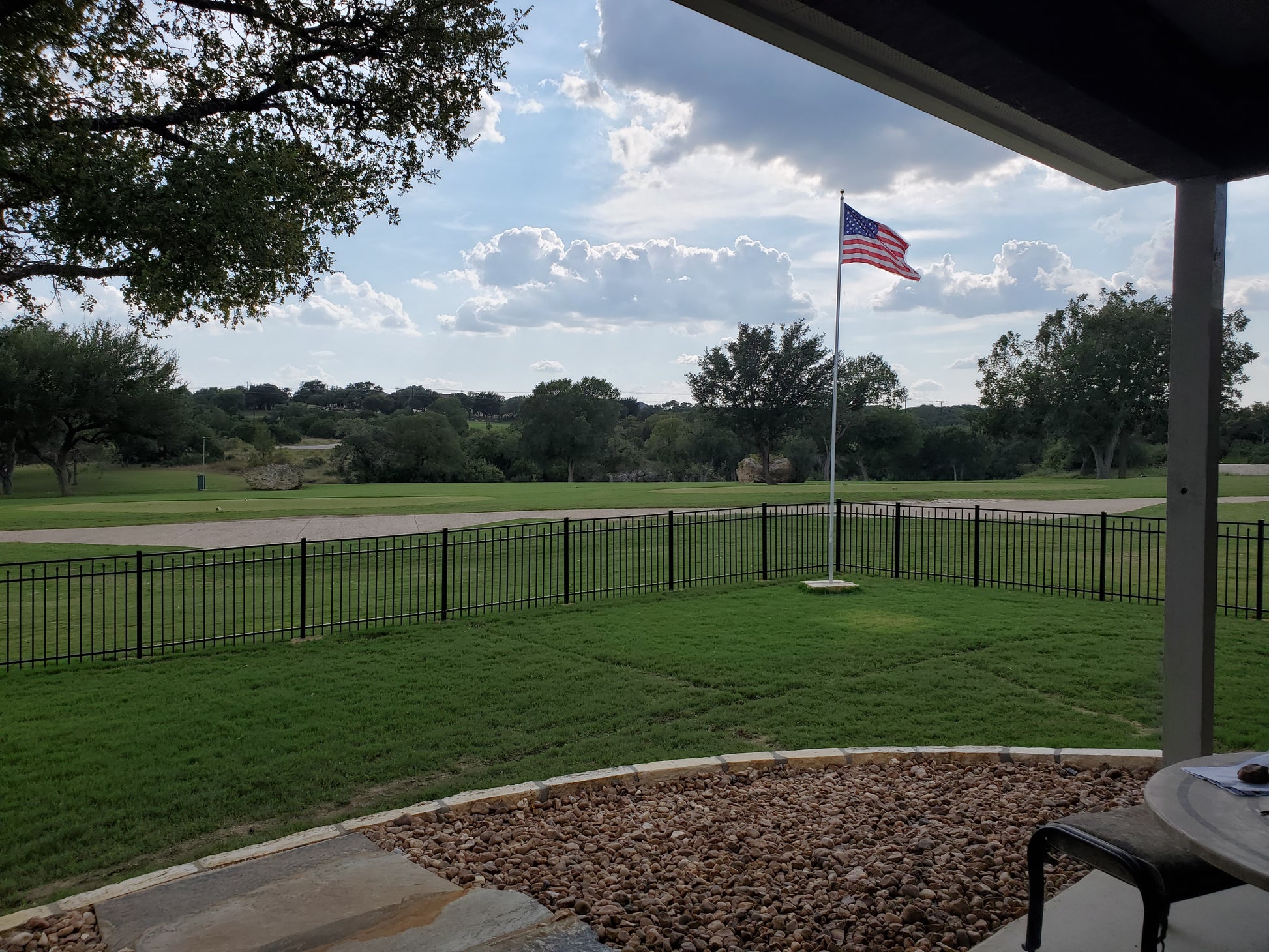American flag on a flagpole in a park with trees and a clear sky behind a Weatherables Toledo black aluminum fencing.