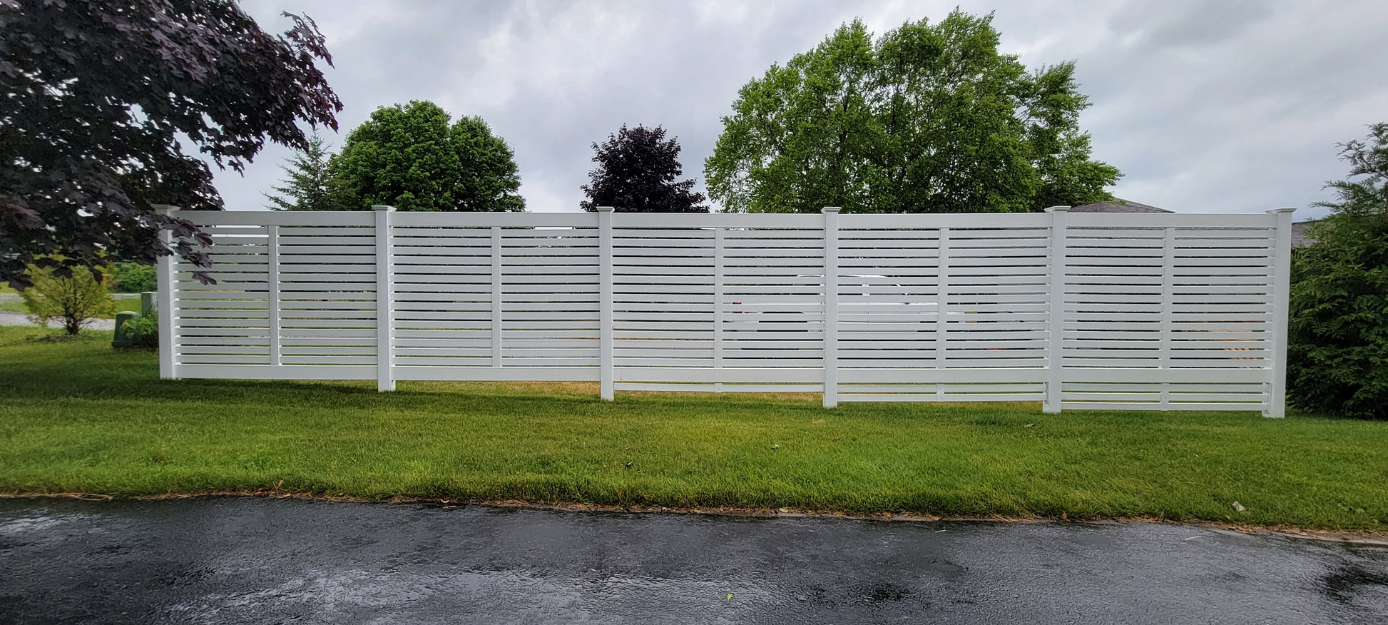 Weatherables Everglade white vinyl semi-privacy horizonal fence in a grassy area with trees in the background