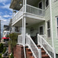 Two-story house with a white porch, Weatherables Greenwich white vinyl deck railing and staircase, surrounded by a street scene.