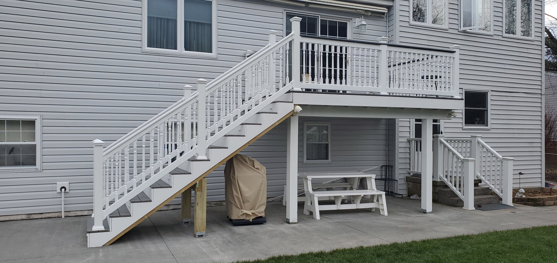 Weatherables Wakefield white vinyl deckboard stair raiiling on a staircase leading to a deck on a gray house
