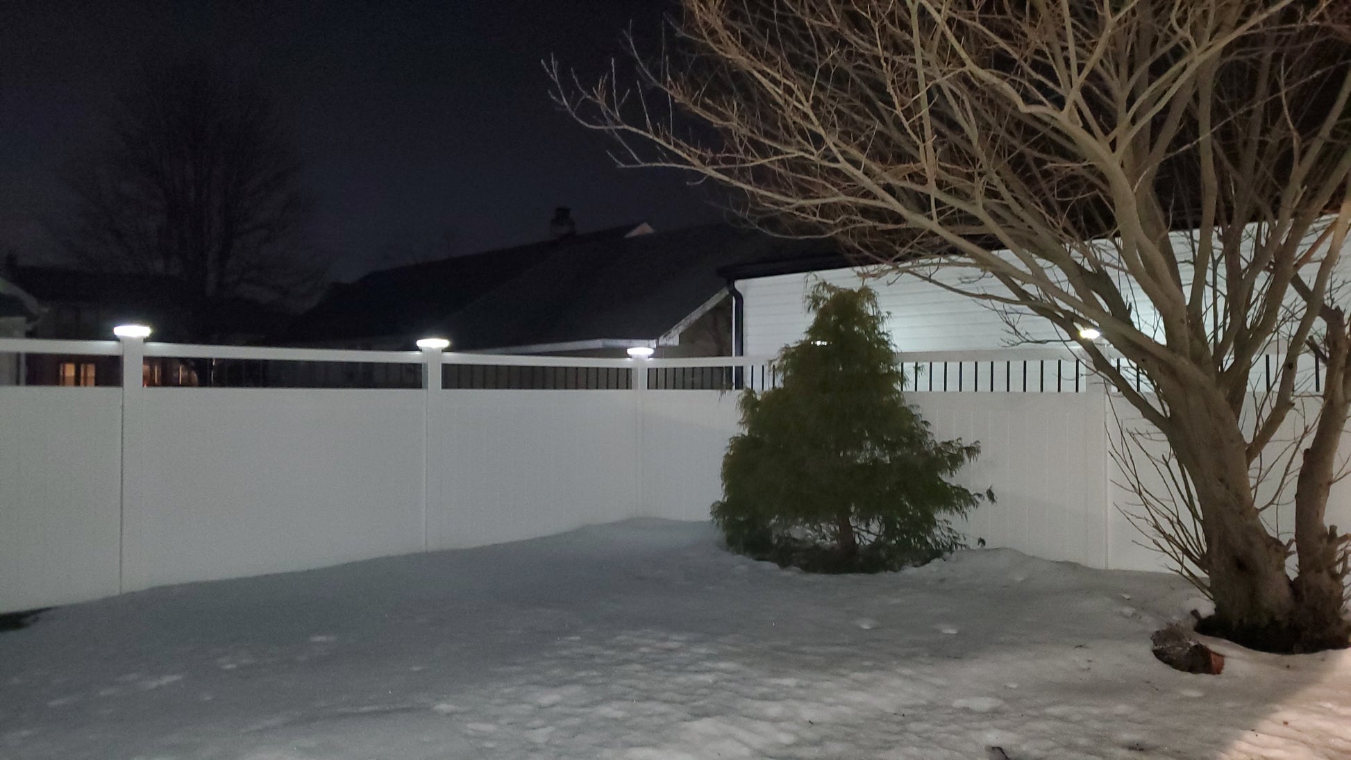 Snowy backyard with a tree and Weatherables Bradford white vinyl privacy fence at night