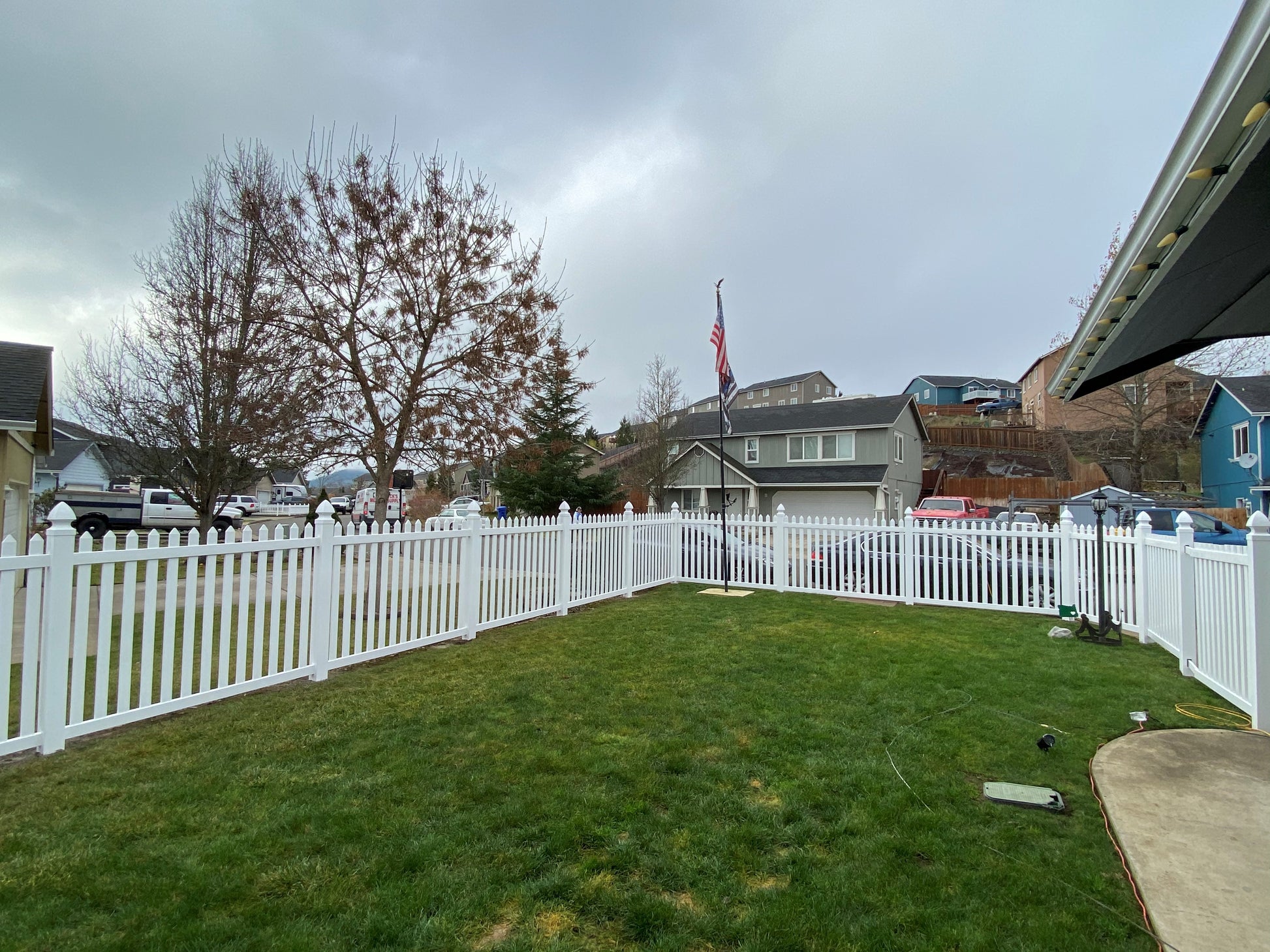 Backyard with Weatherables Chelsea white vinyl picket fence, grass, and a cloudy sky