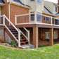 Two-story house with a deck, Weatherables Wiltshire white vinyl dekc and stair railings and stairs leading up to it, surrounded by green grass and shrubs.