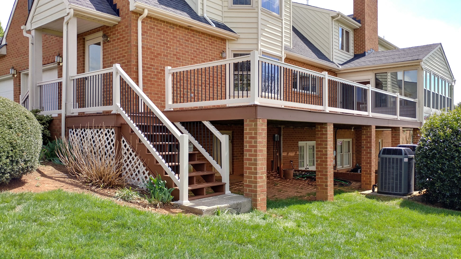 Two-story house with a deck, Weatherables Wiltshire white vinyl dekc and stair railings and stairs leading up to it, surrounded by green grass and shrubs.