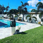 Pool area with potted plants, grass, and a clear blue sky.