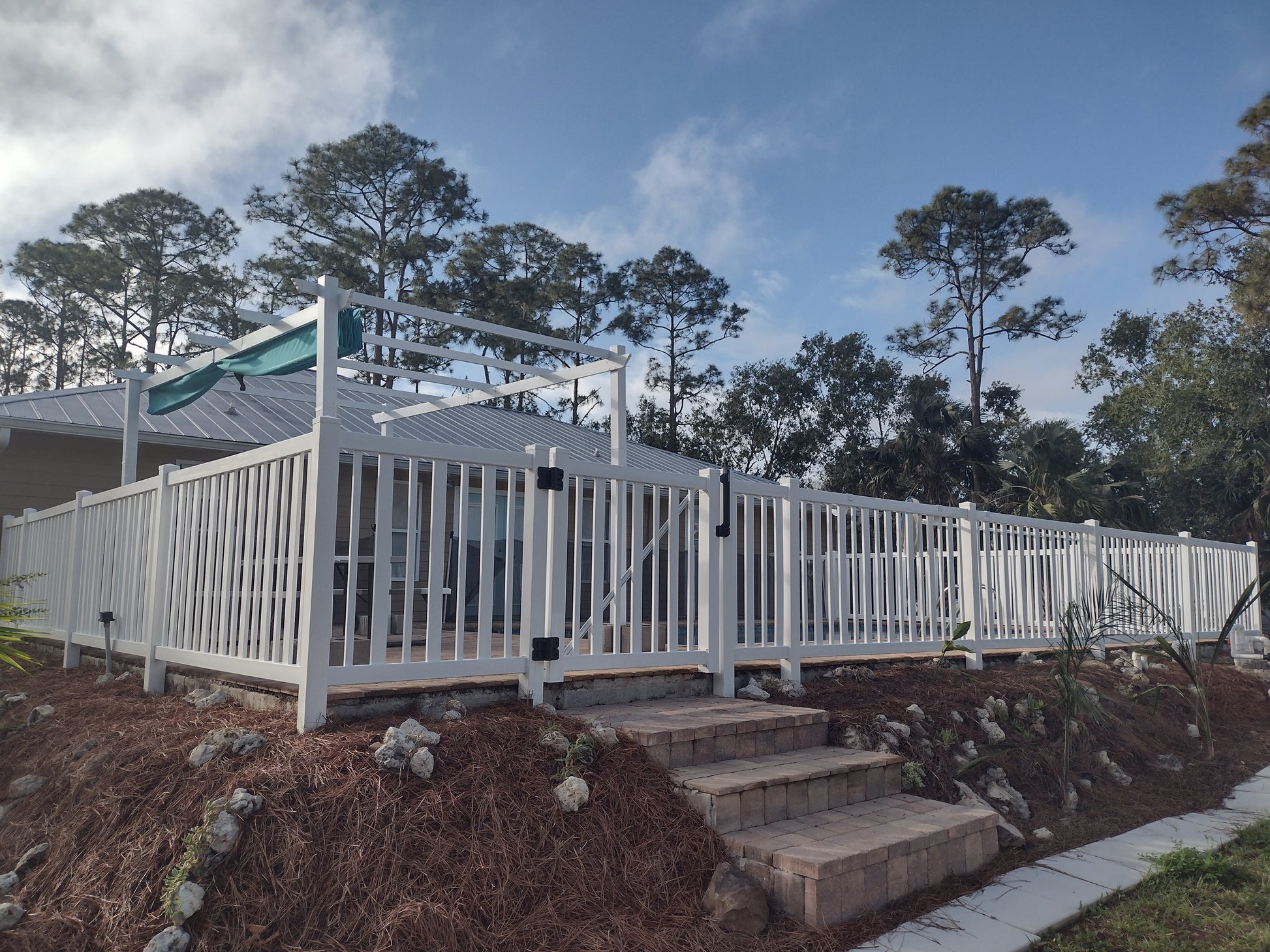 Weatherables Atlantic white vinyl pool fence with steps leading up to it, surrounded by trees and a clear sky.