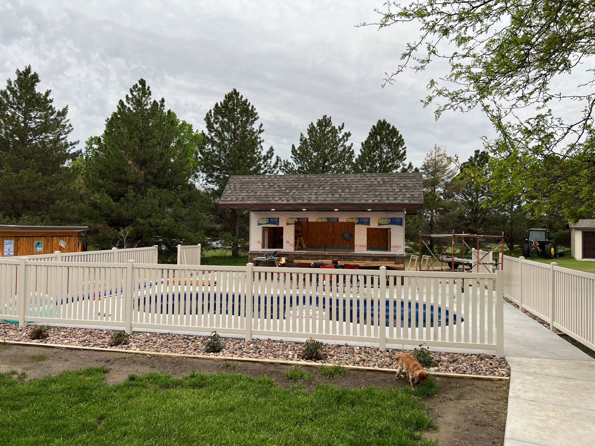 Outdoor playground with a pool, slide, and scaffolding surrounded by Weatherables Crestview tan vinyl pool fence and trees on a cloudy day.