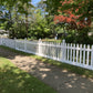 Weatherables Plymouth white vinyl picket fence along a sidewalk with trees and grass in the background