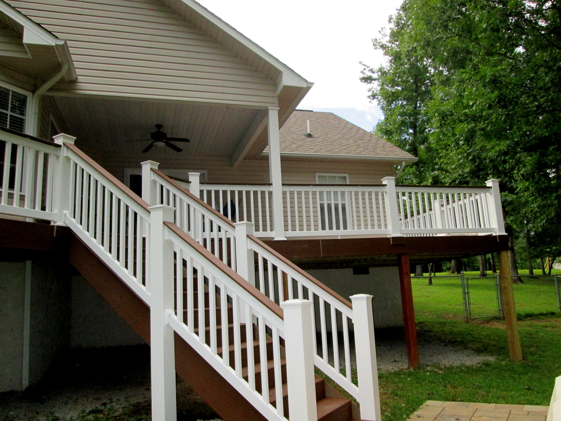 Two-story house with a large deck and Weatherables Bristol white vinyl deck railings, surrounded by trees and greenery.