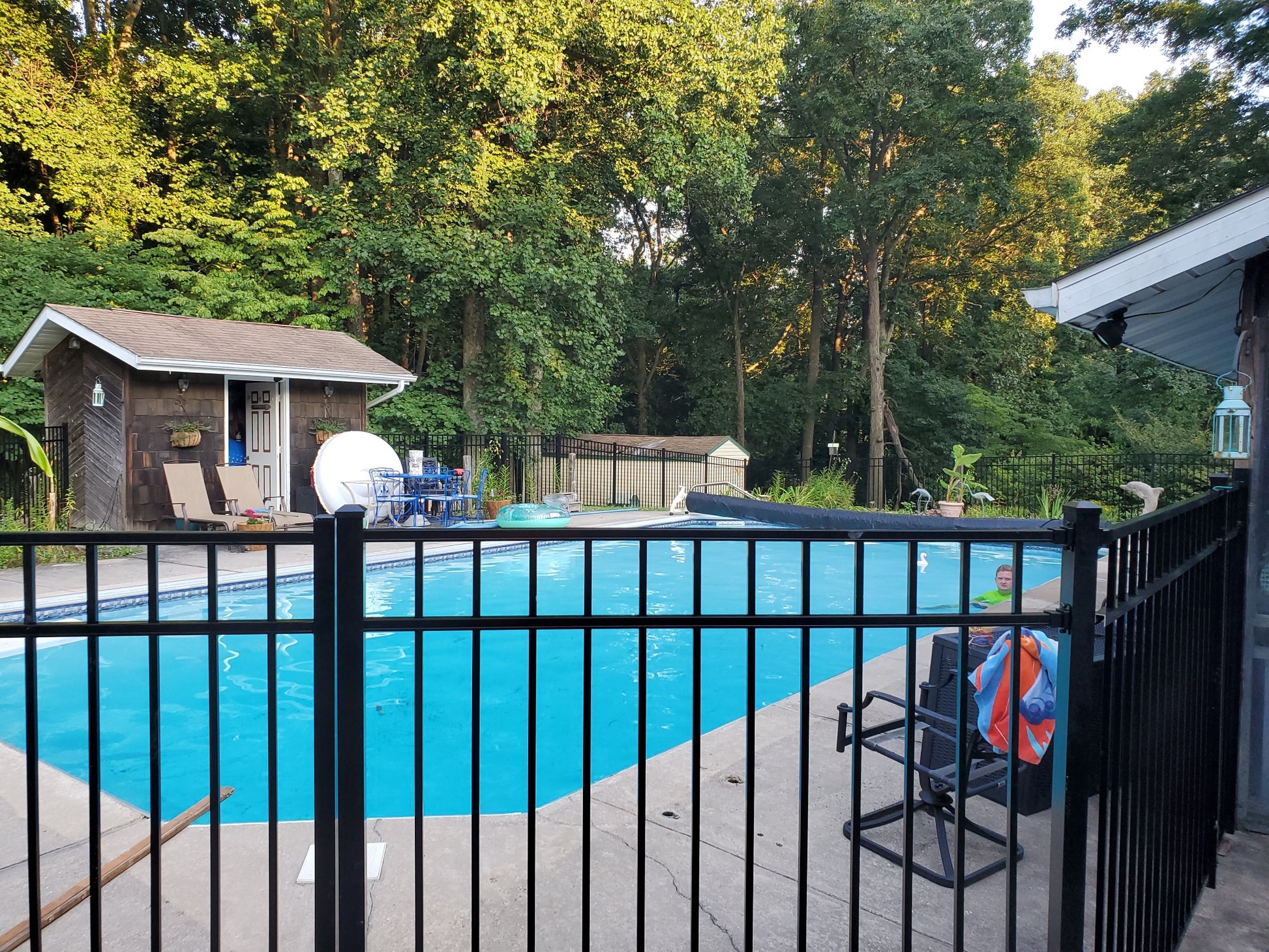 Pool area with a Weatherables Pacific black aluminum fence, chairs, and trees in the background