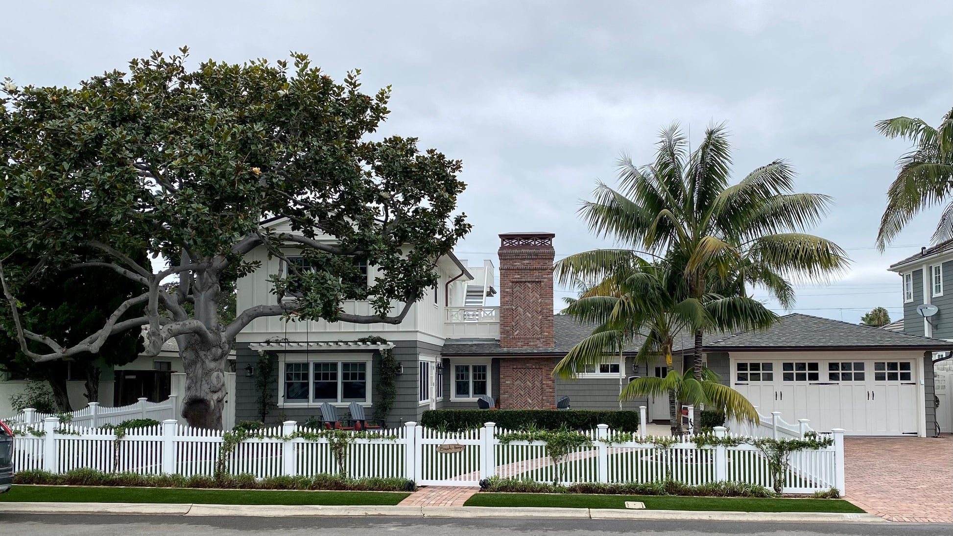 Stylish house with a Weatherables Barrington white vinyl picket fence and palm trees on a cloudy day.