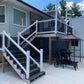 Outdoor patio area with Weatherables Birmingham white vinyl deck railings on stairs leading to a deck, table, chairs, and an umbrella.