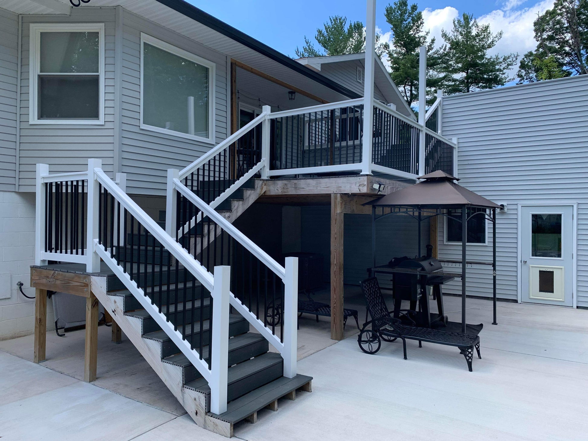 Outdoor patio area with Weatherables Birmingham white vinyl deck railings on stairs leading to a deck, table, chairs, and an umbrella.