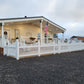 White house with a porch and American flag, surrounded by gravel, Weatherables Barrington white vinyl scalloped picket fence and another building in the background.